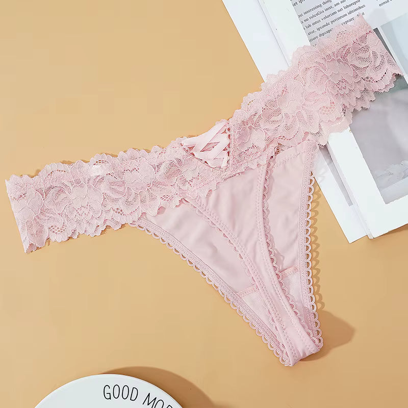 Calcinha rendada rosa clara Lunmiere, detalhe floral em renda, sobre superfície bege.